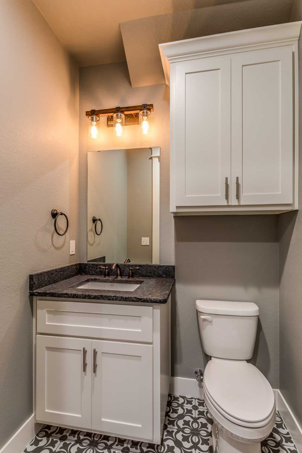 modern small half bath with dimmed yellowish lights, white cabinets, toilet, mirror, and vanity sink